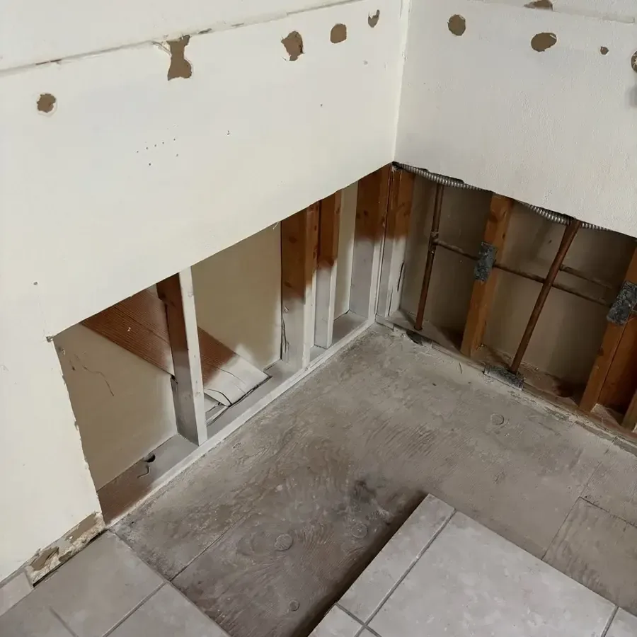Lower wall cavity opened above a tile floor to expose framing and plumbing