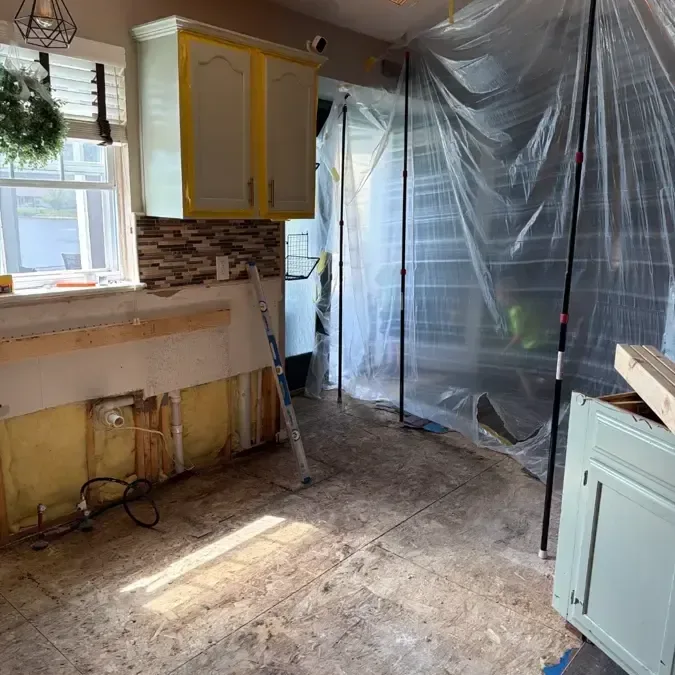 Kitchen with lower cabinets removed and plastic containment across the work area