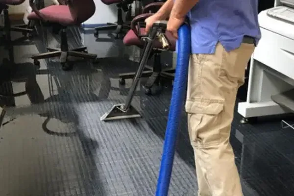 Technician using an extraction wand to remove water from office carpet